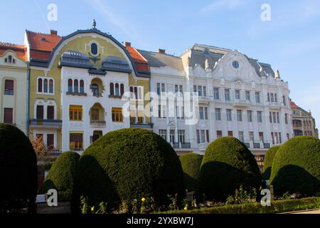 Charming Art Nouveau buildings in Timisoara, Romania, with colorful facades, decorative details, and lush greenery under a bright blue sky. Stock Photo