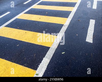 yellow painted striped footpath drawn on black freshly laid asphalt road surface in autumn rainy day Stock Photo