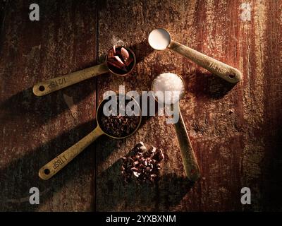 Golden Measuring Spoons with Ingredients Chocolate Cocoa Sugar Milk on distressed wooden backdrop dramatic lighting Stock Photo