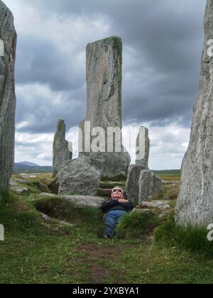 Man lying down pretending to be in a grave pit at Callanish standing stones, Isle of Lewis, Outer Hebrides, Scotland, UK Stock Photo