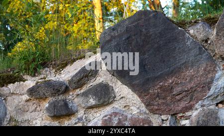 Close-up of an ancient stone wall fragment, partially overgrown with wild grass and plants. The texture of the stones and the natural overgrowth highl Stock Photo