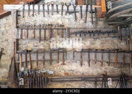 Traditional blacksmith tools on a rustic stone wall in a blacksmith shop Stock Photo