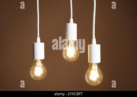 Light bulbs hanging on cords against brown background Stock Photo