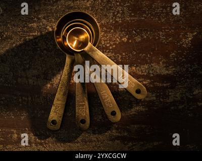 Golden Measuring Spoons with Ingredients Chocoltae Cocoa Sugar Milk on distressed wooden backdrop dramatic lighting Stock Photo