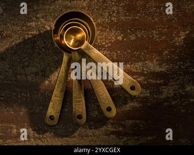 Golden Measuring Spoons with Ingredients Chocoltae Cocoa Sugar Milk on distressed wooden backdrop dramatic lighting Stock Photo