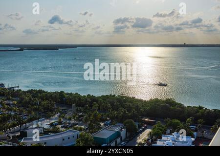 Scenic view of Caribbean Sea reflecting sunlight, with boat sailing near lush green coastline and tropical resort buildings. Cancun. Mexico. Stock Photo