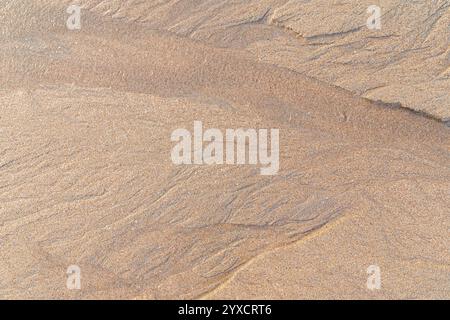 Abstract shapes and patterns in the grainy sand and flowing water on the beach on a sunny day, viewed from above. Textured natural sandy background. Stock Photo