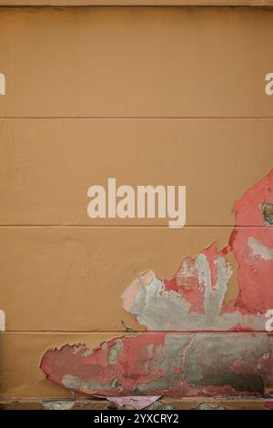 Front view of a wall painted in orange. Paint is partly peeled off revealing pink paint and raw concrete. Abstract full frame textured background. Stock Photo