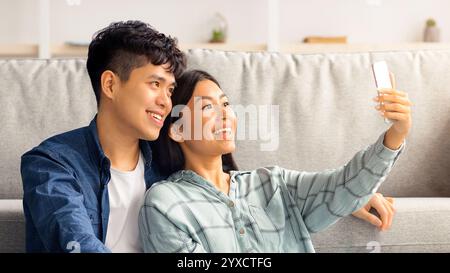 Loving chinese couple with cleaning tools taking selfie, using smartphone Stock Photo