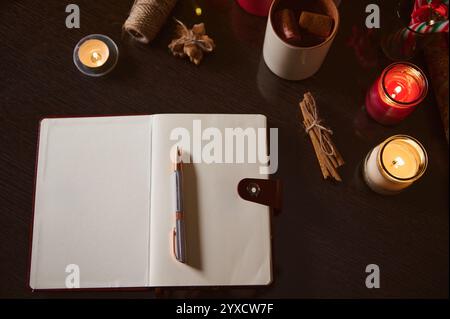 An inviting work setup featuring an open notebook, pen, candles, and a cup of cocoa, perfect for creative writing or journaling. Stock Photo