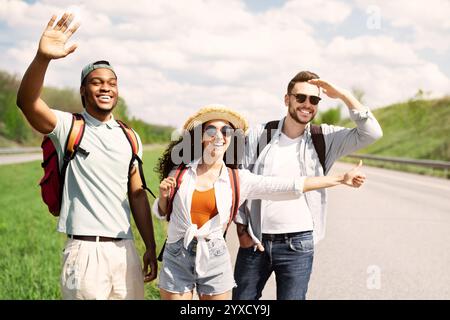 Millennial people standing on roadside, stopping car, trying to get free ride, having autostop journey, copy space Stock Photo