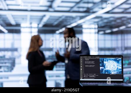 Focus on AI software on laptop in front of coworkers programming in AI data center. Close up of notebook in Server hub used by workers upgrading artificial intelligence systems Stock Photo