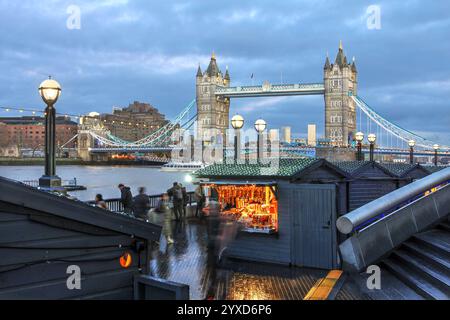 London Tower Bridge looming over Christmas Market by the River, United Kingdom at sunset. Stock Photo