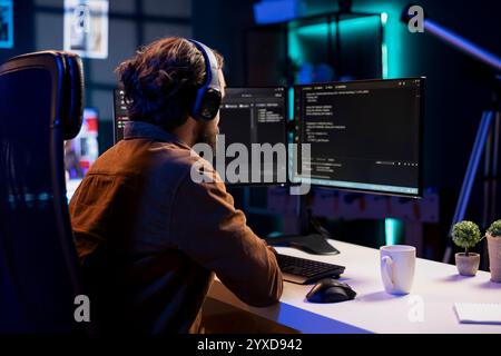 Man listening music while doing software quality assurance, reading source code on computer screen. Developer wearing headphones enjoying podcasts and inspecting coding on desktop PC Stock Photo