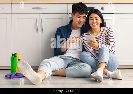 Tired asian man and woman sitting on floor, using phone Stock Photo