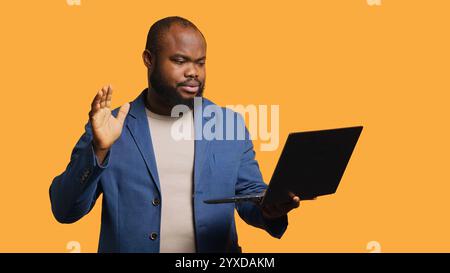 Employee does no hand gesture with finger while chatting with coworker during meeting using laptop, studio background. Person showing disagreeing sign, protesting idea during videocall, camera A Stock Photo