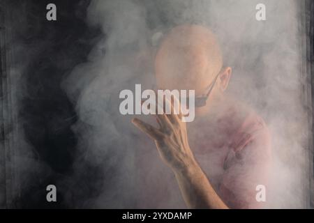 Bald and bearded man making expressions with his head down in a studio with a smoky black background. South American Stock Photo