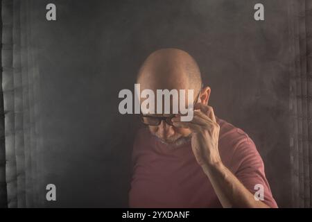 Bald and bearded man making expressions with his head down in a studio with a smoky black background. South American Stock Photo