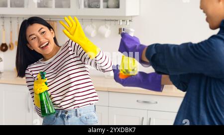 Playful asian lovers having fun while cleaning house together Stock Photo