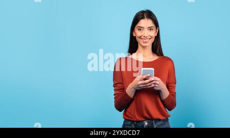 Woman smiling while using smartphone against bright blue background Stock Photo