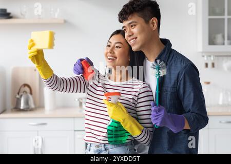 Cute asian couple taking selfie with sponge while cleaning kitchen Stock Photo