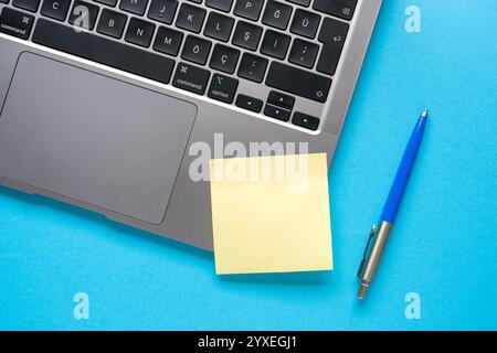 Top view of blank sticky note stuck on laptop on blue table Stock Photo
