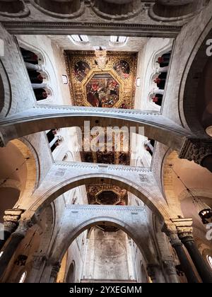 Bari, Italy - July 18, 2022: View of ornate gold ceiling and stone arches inside a historic cathedral, showcasing detailed artwork and architectural g Stock Photo