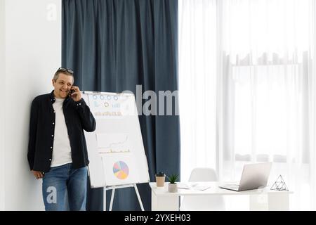 A man dressed in casual clothes works in the office and holds a mobile phone. The man works in a remote place of work Stock Photo