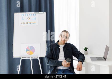 A man dressed in casual clothes works in the office with a laptop and expresses positive emotions. The man works in a remote place of work Stock Photo
