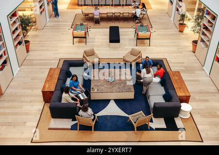 An overhead shot of a contemporary office lounge featuring diverse individuals working and socializing. The comfortable seating arrangements promote c Stock Photo