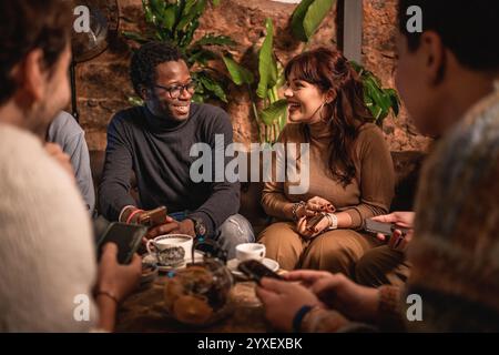 Young diverse group enjoying social time at trendy cafe, sharing smartphone content while drinking coffee. Modern friendship blending digital and real Stock Photo