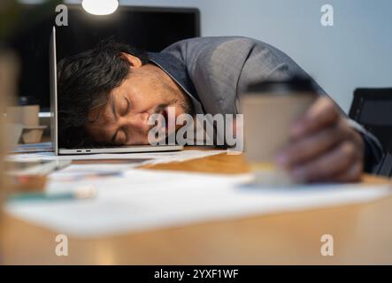 Asian tired staff officer man sleeping while using desktop computer having overwork project overnight in office. Selective focus. Stock Photo