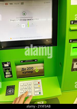 Kyiv, Ukraine - December 15, 2024: Person using an ATM machine by entering the PIN code to securely access banking features. Green interface and keypa Stock Photo