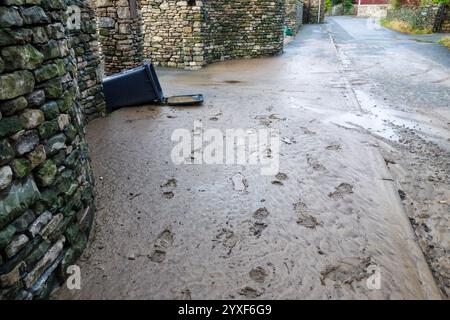 Footprints in mud and silt left on a footpath after a flooding due to a fierce storm - a wheelie bin is shown upturned. Concept: disaster, damage Stock Photo