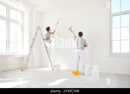 Two painters in uniform paint the walls white, back view Stock Photo