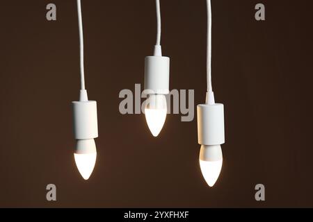 Light bulbs hanging on cords against brown background Stock Photo