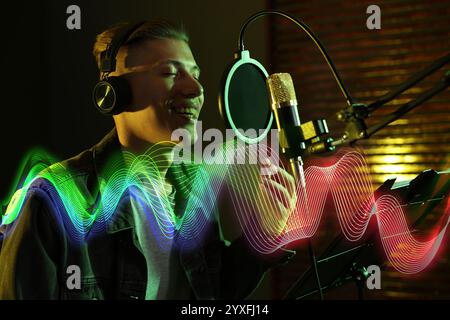 Vocalist with headphones singing into microphone in professional record studio. Sound waves Stock Photo
