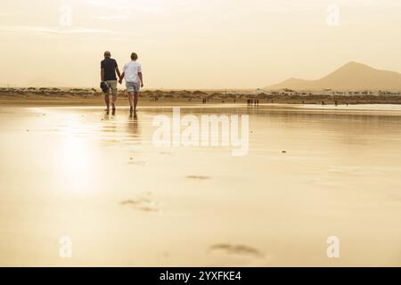 Back view of active senior couple walking on a beach in the golden sunset in Canary Islands Stock Photo