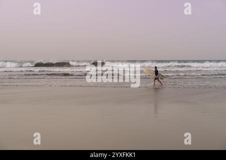 Surfer with surfboard in hands going through beautiful sand beach in Lanzarote, Canary Islands Stock Photo