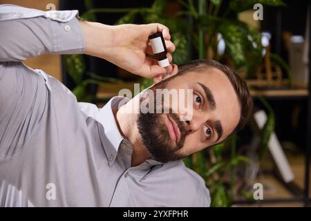 Young man suffering from ear pain and puts ear drops in them while sitting at work. Diseases and treatment. Stock Photo