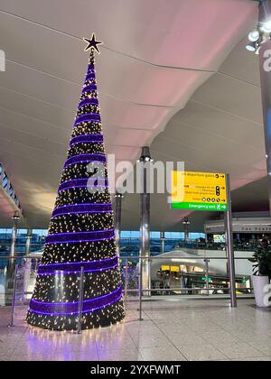 Inside Heathrow terminal 2 Christmas tree decorated in purple and white lights. No people. Stock Photo