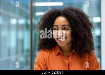 Portrait of a cheerful young woman with glasses, sitting in a modern office setting. Stock Photo