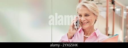 Website header shot of smiling mature businesswoman talking on phone in hallway of modern coworking space, copy space Stock Photo
