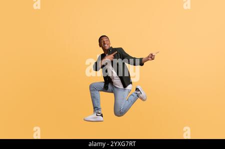 Joyful young man jumping in excitement against a bright yellow background Stock Photo