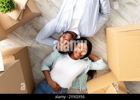 Loving african american couple lying among cardboard boxes on floor of their new apartment, top view Stock Photo