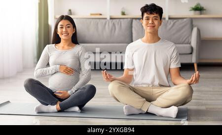 Positive pregnant asian couple doing yoga together Stock Photo