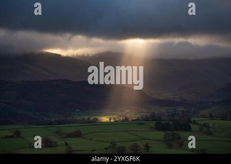 Beams of sunlight breaking through dramatic clouds over green fields in the British countryside. Keswick, Lake District, UK. Stock Photo