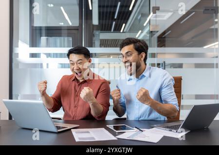 Two enthusiastic professionals celebrate a victory while working together in office. Their expressions convey excitement and teamwork, making it a dynamic and uplifting moment. Stock Photo