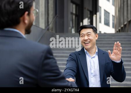 Two business professionals exchanging a friendly handshake and warm smile an outdoor urban setting. The scene captures the essence of professional courtesy, networking, and successful collaboration Stock Photo