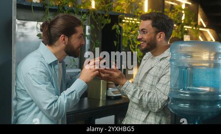 Arabian man drink water cooler in office coffee break pause two business men multiethnic businessmen colleagues coworkers Caucasian Indian guys Stock Photo